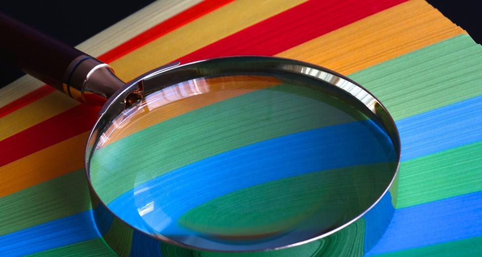 Afbeelding: vergrootglas op kleurig gestreepte ondergrond